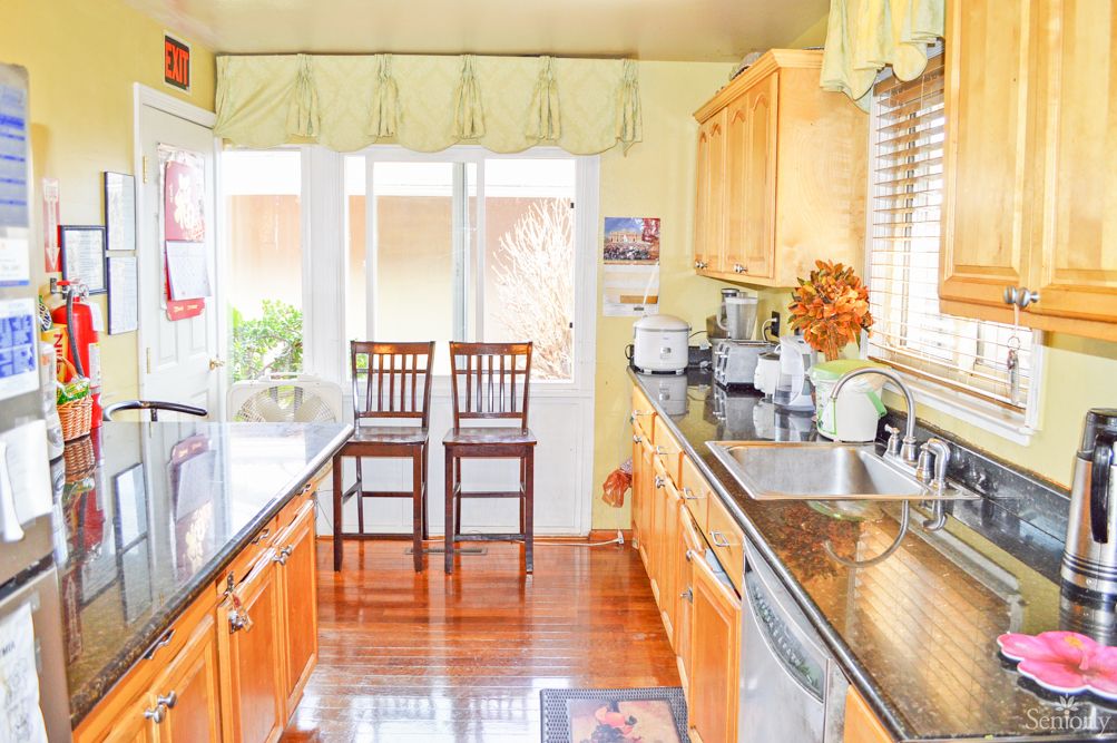 A bright kitchen featuring wooden cabinets, granite countertops, and two high chairs by the window.