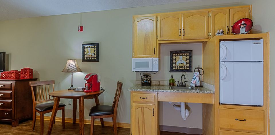 A cozy kitchenette with wooden cabinets and a small dining area, featuring a red coffee maker.
