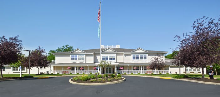 A large building with a flagpole and landscaped entrance under a clear blue sky.