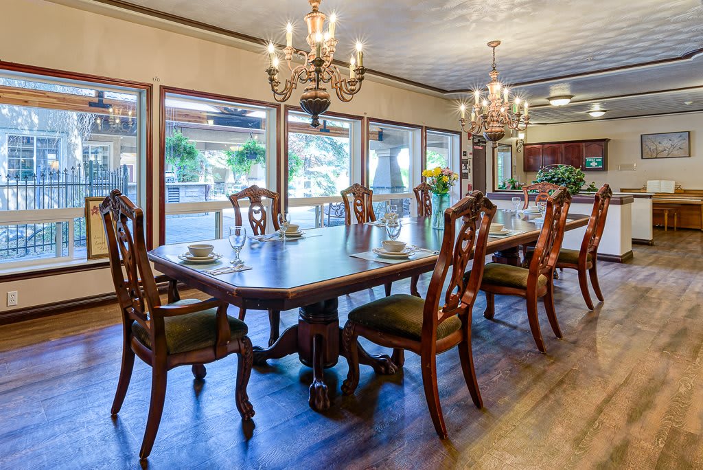 An elegant dining room featuring a large wooden table, ornate chairs, and grand chandeliers with abundant natural light from the windows.
