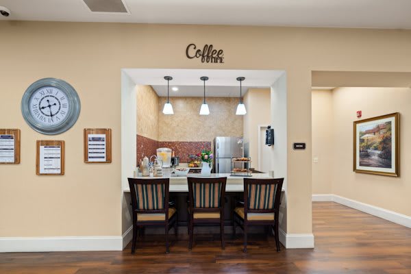 A cozy coffee station with a countertop and chairs, featuring pendant lights and a small kitchenette area.
