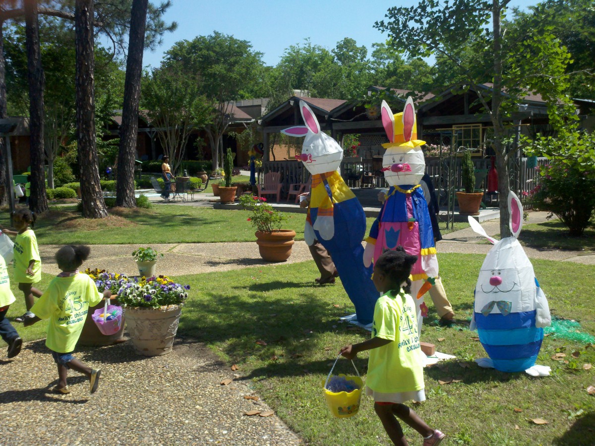Children participate in an Easter egg hunt outside, surrounded by colorful bunny decorations.