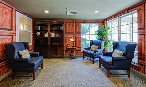 A cozy living room with blue chairs, a wooden bookshelf, and a warm atmosphere.