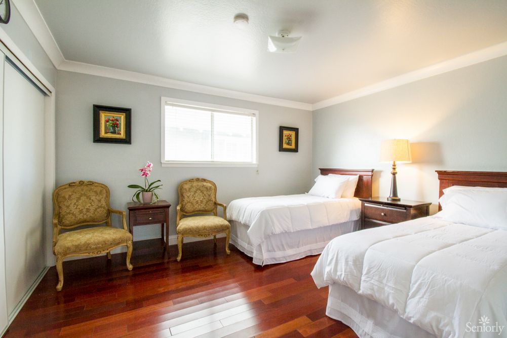 A cozy bedroom with two single beds, wooden floors, and ample natural light.