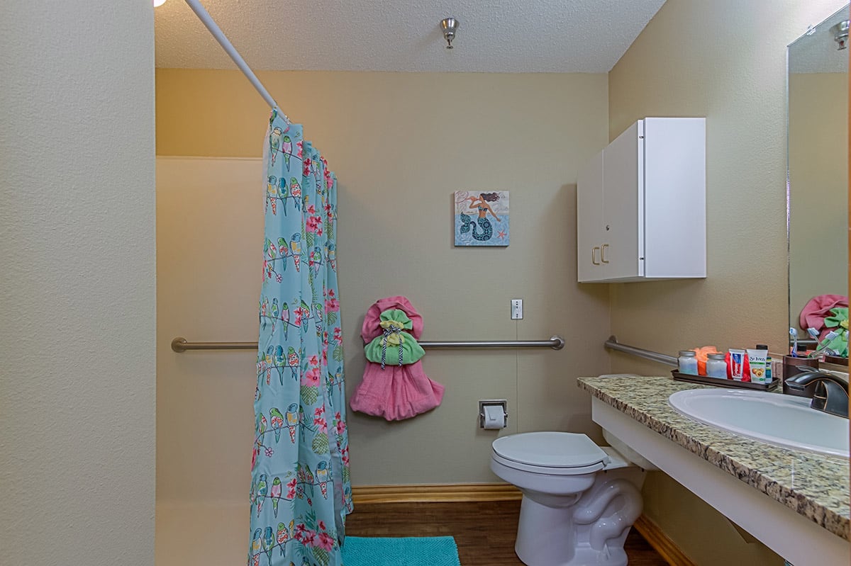 A brightly decorated bathroom featuring a shower with a colorful curtain, a toilet, and a sink.