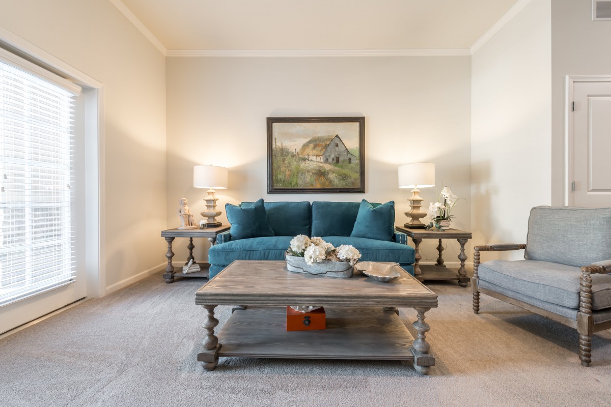 A cozy living room with a teal sofa, wooden coffee table, elegant artwork, and decorative lamps.
