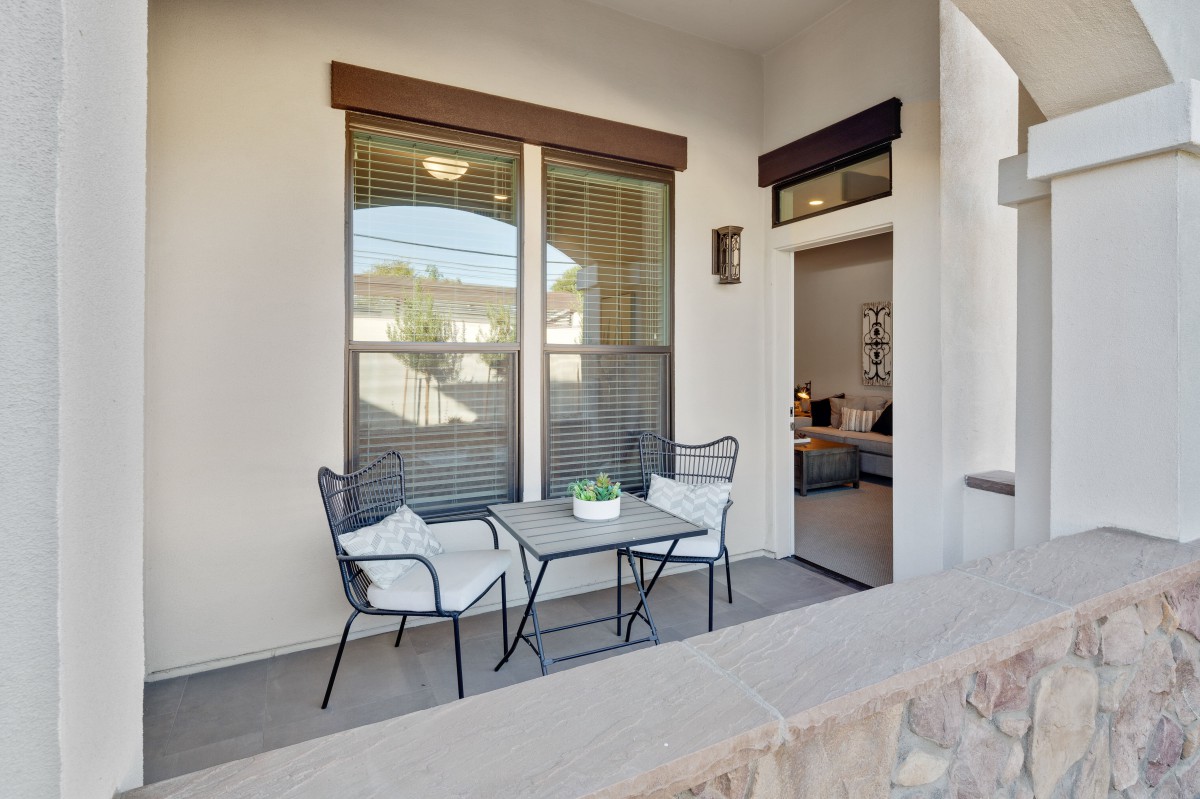 A cozy patio area with a small table and two chairs adorned with cushions, accompanied by a potted plant, situated next to a large window and an open doorway.