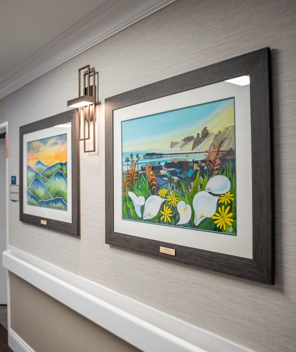 Framed paintings displayed in a well-lit hallway.