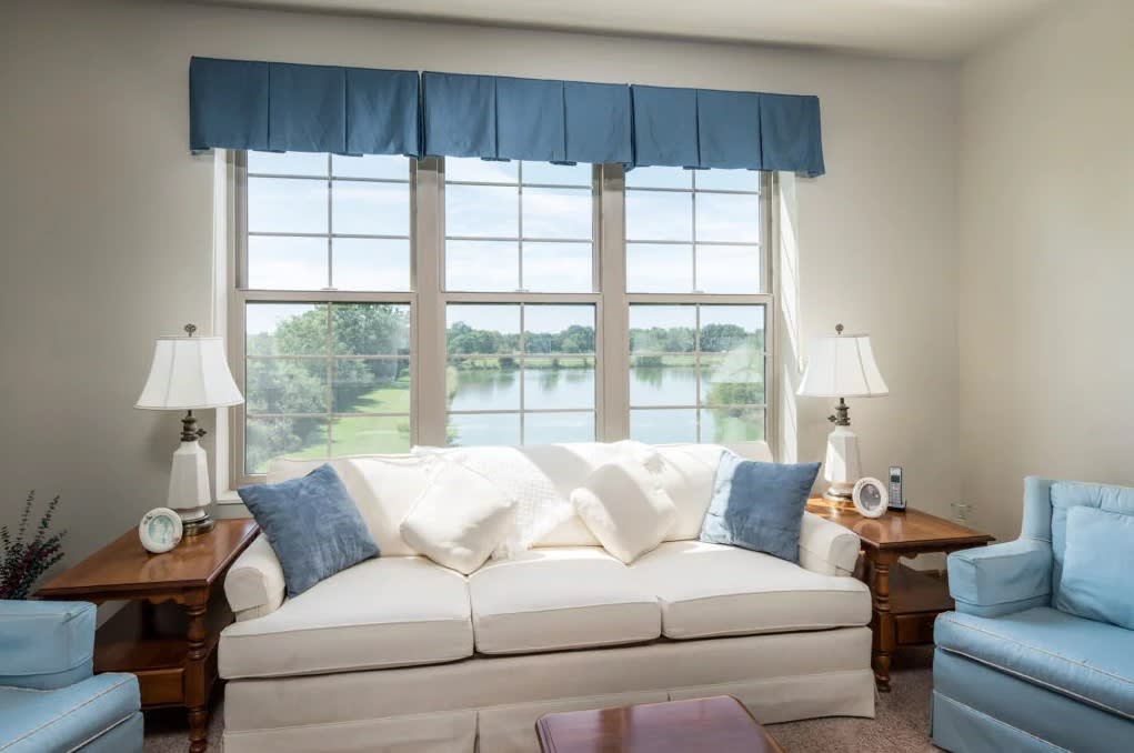 A cozy living room with a white sofa, blue pillows, and ample natural light streaming through the large window.