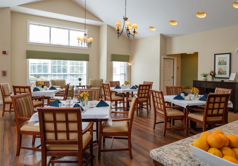 A bright and inviting dining room featuring neatly arranged tables and chairs, illuminated by natural light through large windows.