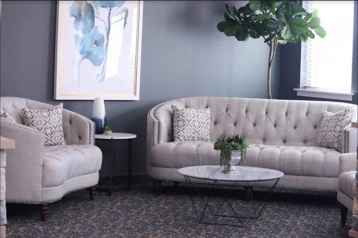 A modern living room featuring elegant sofas, a round coffee table, abstract artwork, and a large potted plant.