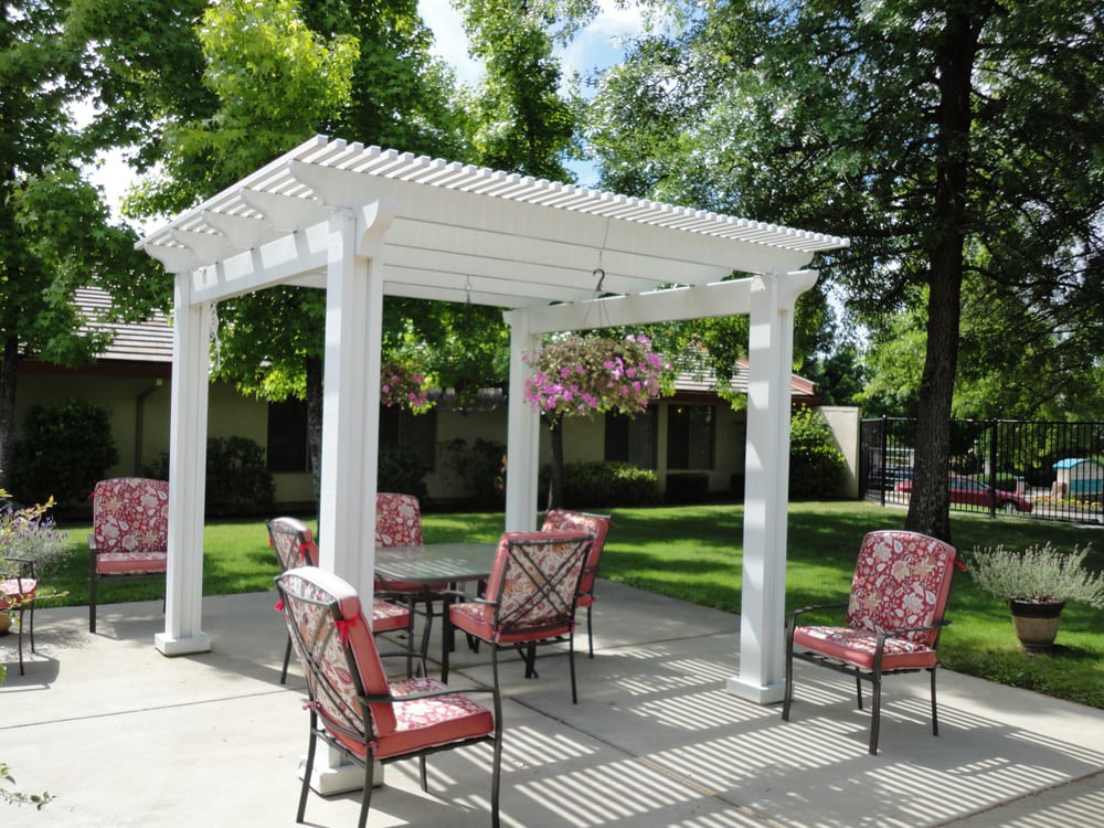 A beautiful outdoor patio area featuring a white pergola with hanging plants and comfortable seating.