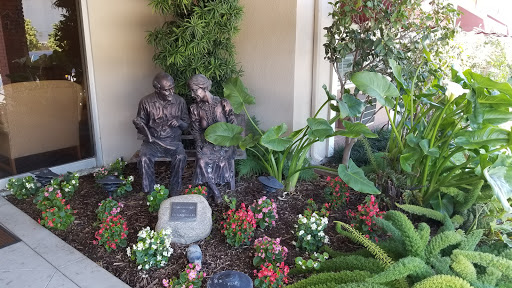 A serene garden scene featuring two statues seated among vibrant flowers and lush greenery.
