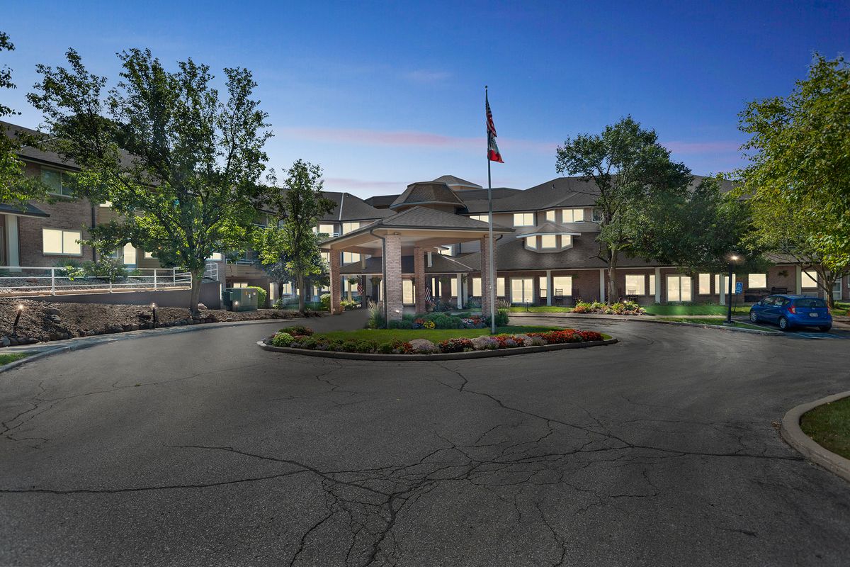 An elegant building with a circular driveway, surrounded by trees and lit up in the evening.