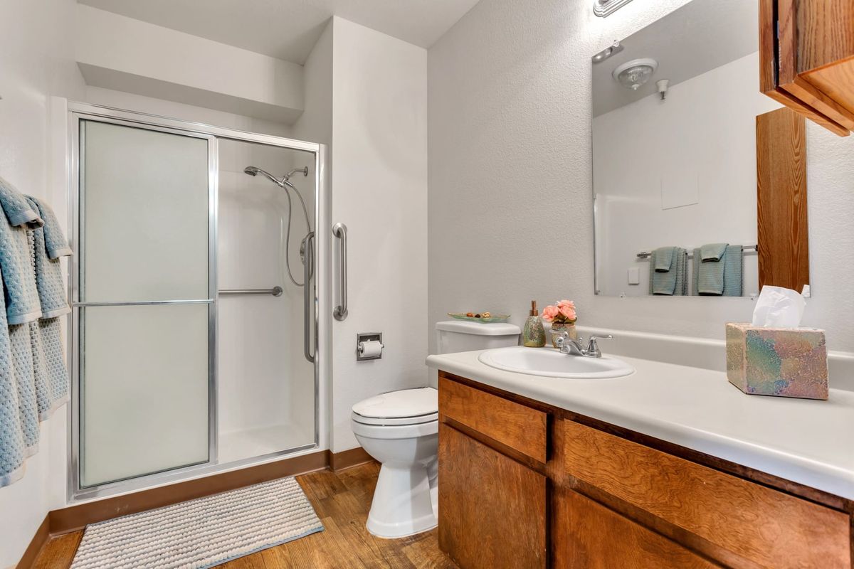 A modern, well-lit bathroom featuring a shower, toilet, and sink with wooden cabinets.