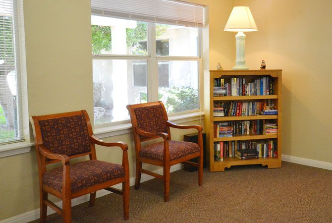 A cozy waiting room with two chairs, a bookshelf, and a lamp by the window.