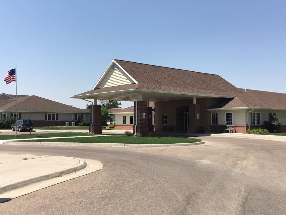 A building with an entrance featuring an awning and a circular driveway on a sunny day.