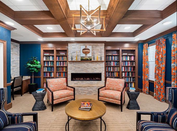 A cozy library room with a modern design featuring bookshelves, armchairs, and a fireplace.