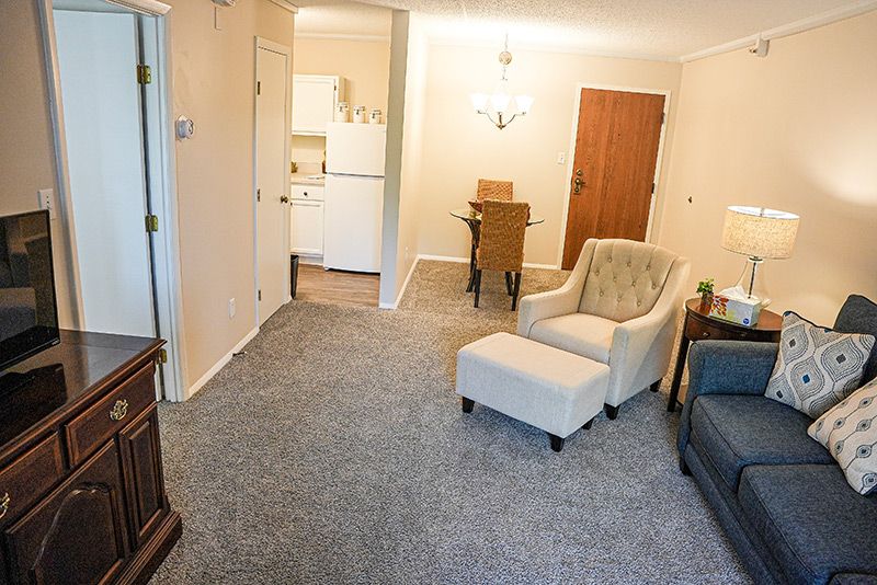 A cozy living room with an armchair, carpeted floor, and a view of the dining area.