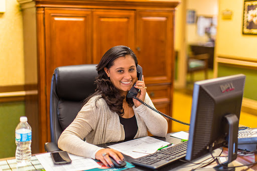 A cheerful woman working in an office, engaged in a phone call while sitting at her desk.