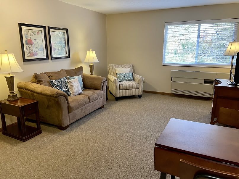 A cozy living room with a sofa, armchair, and a warm lamp by the window.