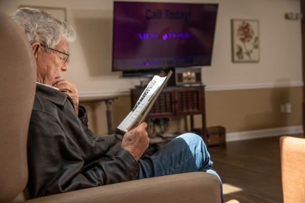 An elderly man is reading on a tablet while seated in a cozy living room.