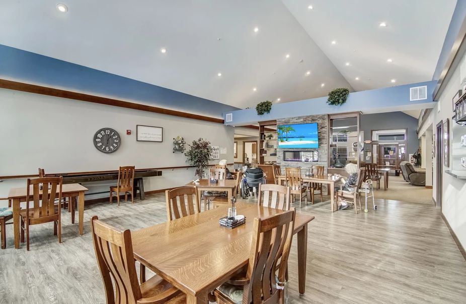 A modern dining area with wooden tables and chairs, featuring a television and decorative wall art.