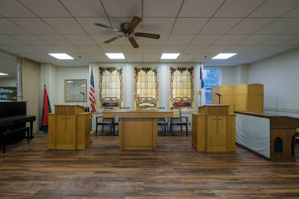 A courtroom interior featuring wooden furniture, flags, and a wooden floor.