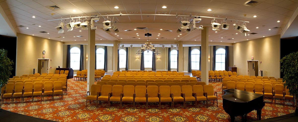 An empty conference room with rows of yellow chairs and projectors, ready for an event.