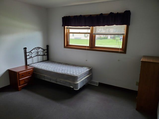 A minimalist bedroom featuring a single bed with a mattress, positioned beside a window.