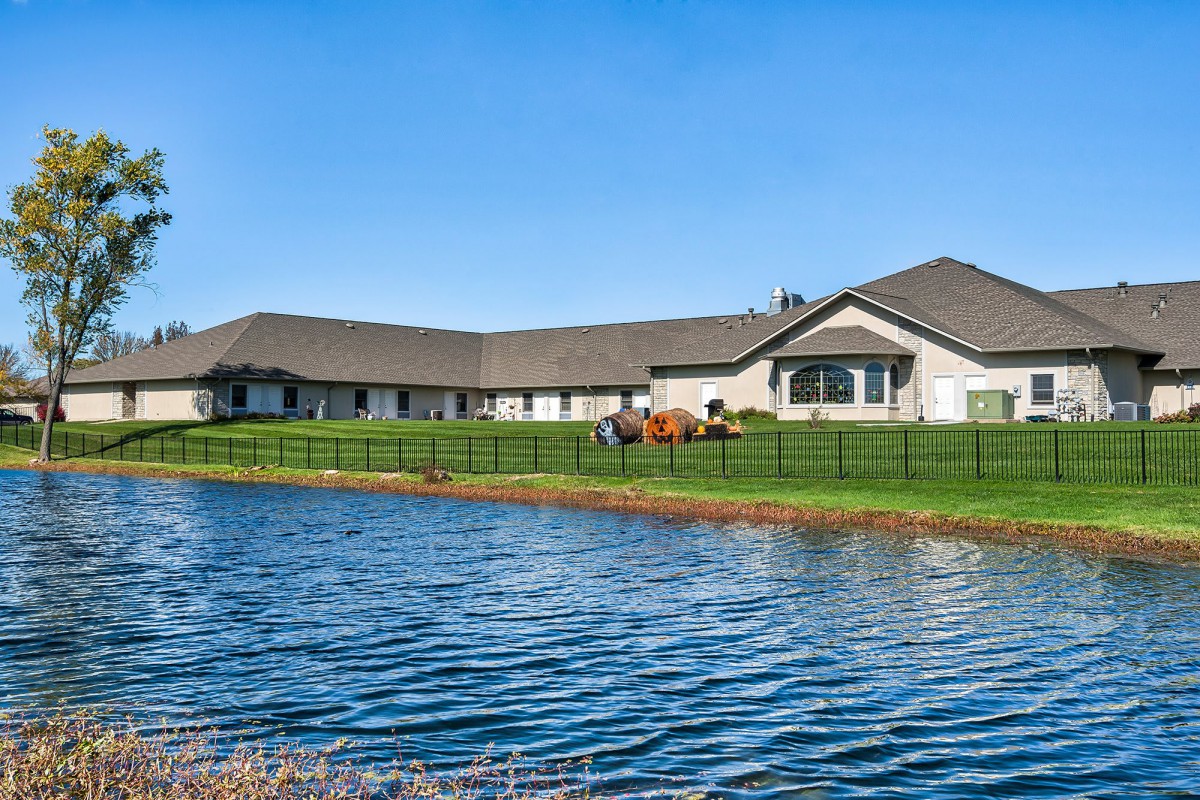 A large house with a well-maintained green lawn situated by a lake under a clear blue sky.