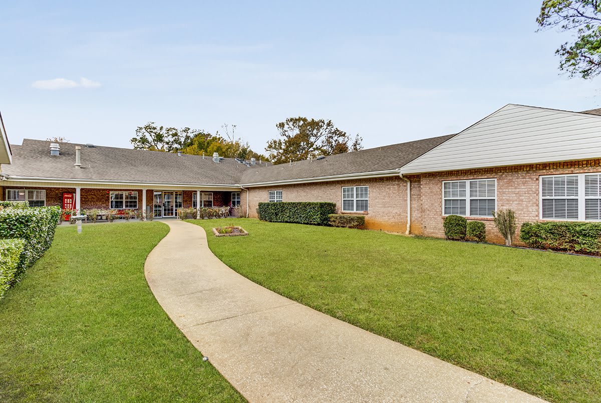 A single-story residential building with a well-maintained lawn and a curved pathway in front.