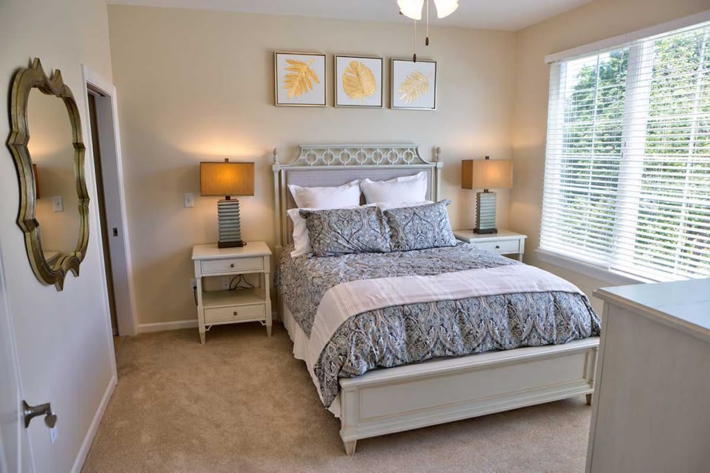 A modern bedroom with a neatly made bed, flanked by nightstands and lamps, decorated with artwork above the headboard.
