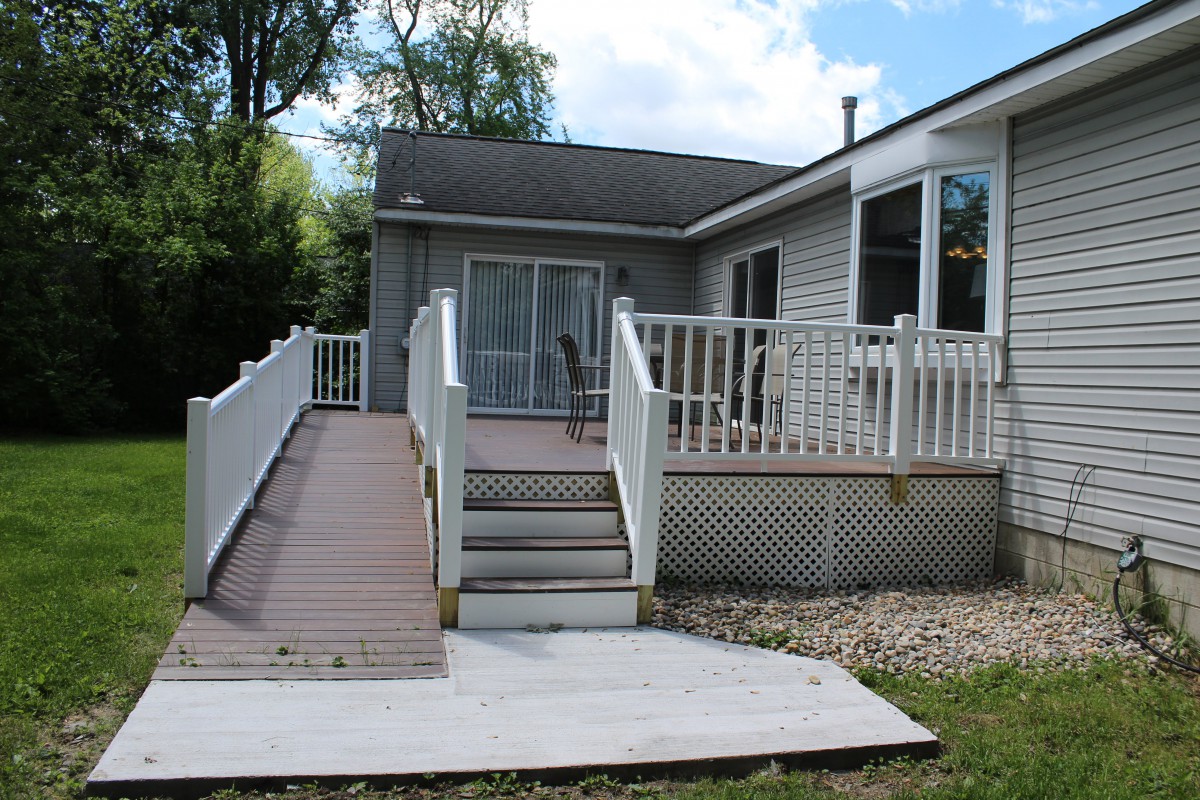 A house with a wooden deck featuring both stairs and an accessibility ramp.