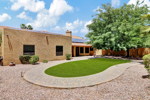 A beautifully landscaped residential home featuring a spacious lawn and patio area, under a clear blue sky.