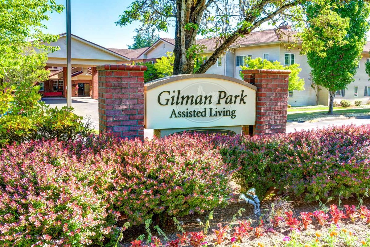 Entrance sign for Gilman Park Assisted Living surrounded by greenery.
