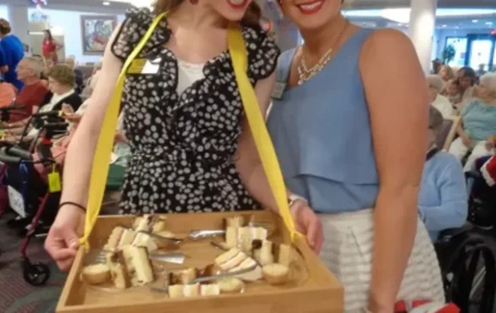 Two women holding a tray with assorted cheeses at an event.