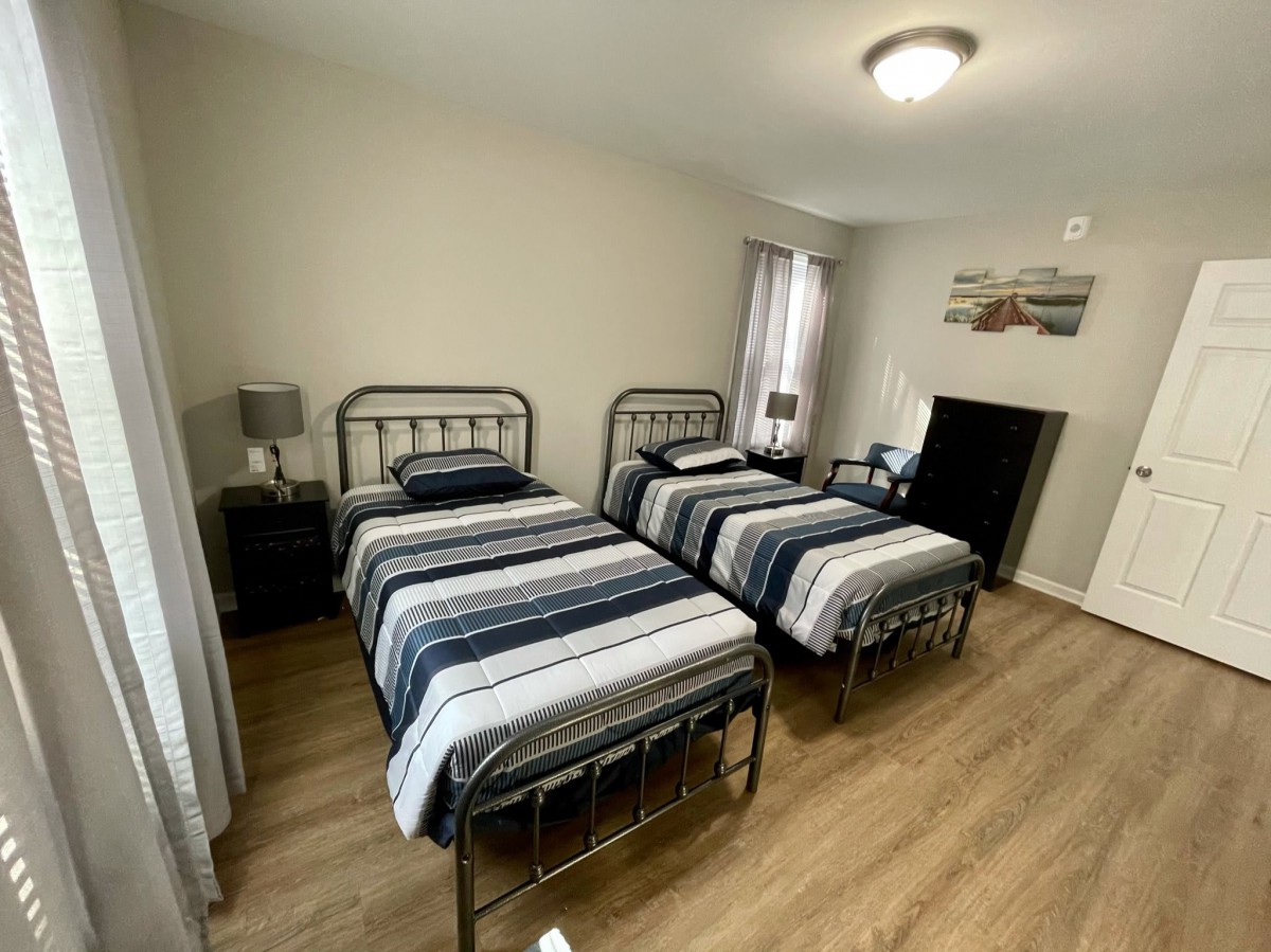 A cozy bedroom with two twin beds featuring striped bedding and metal bed frames on wood flooring.