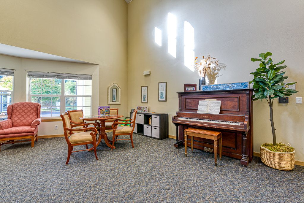 A cozy living room with a piano, table, and chairs near a large window.