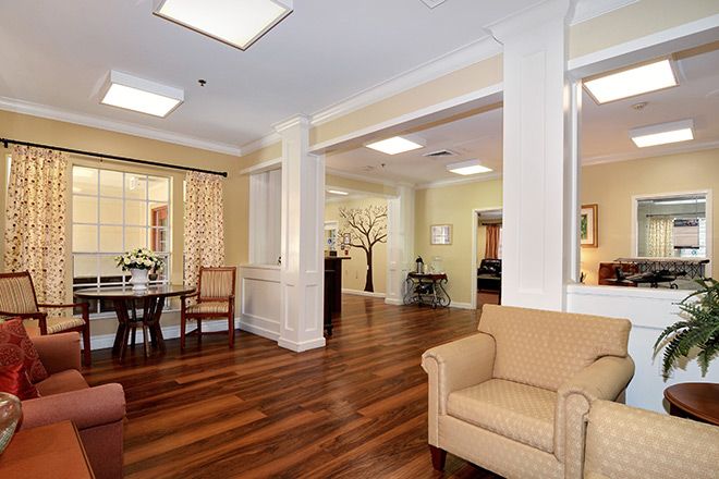 A well-lit living room with wooden flooring, featuring a comfortable sofa and a dining area in the background.