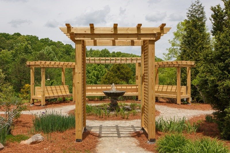 A beautiful garden featuring a wooden pergola and a central fountain.