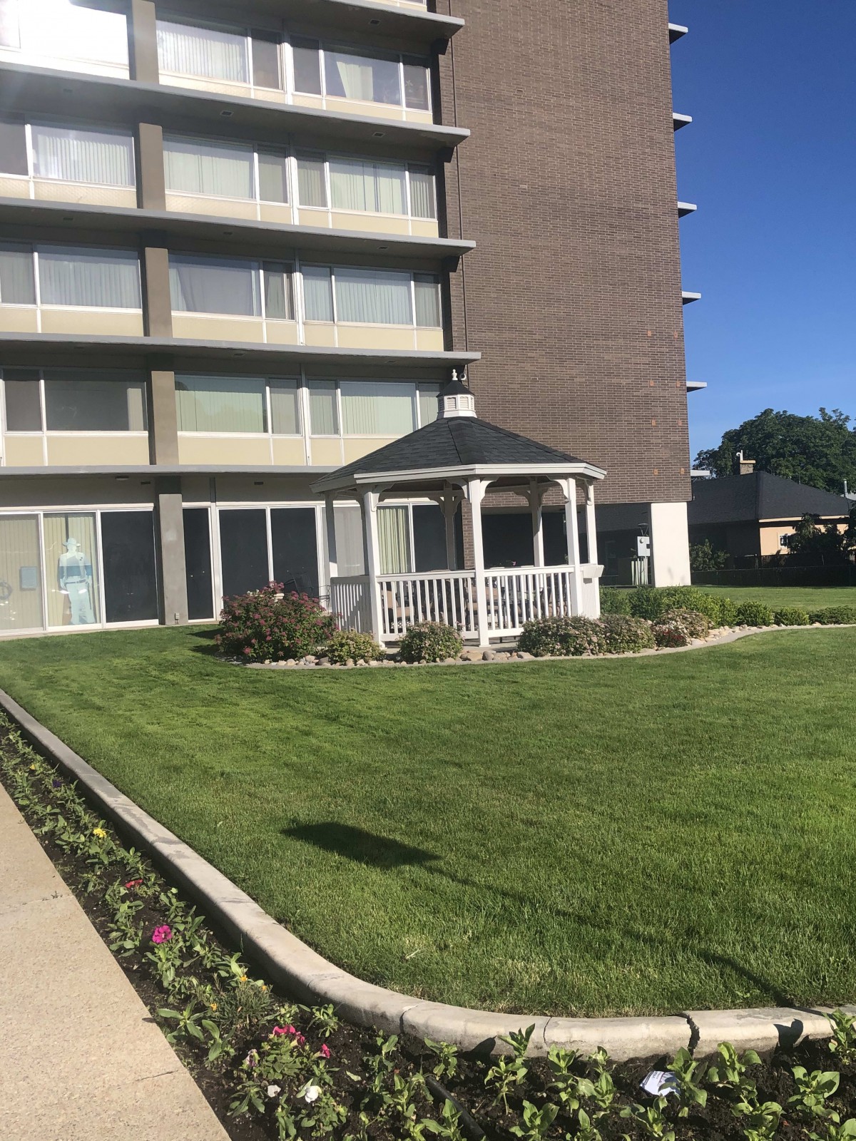 A well-maintained lawn with a gazebo in front of a multi-story building.