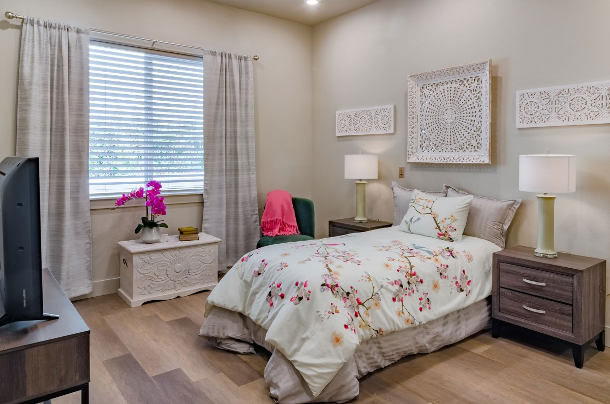 A cozy bedroom with a single bed featuring floral bedding, complemented by a nightstand and decorative wall art.