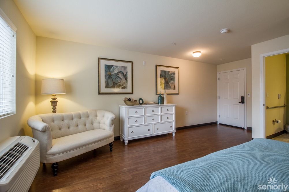 A cozy bedroom with elegant decor, featuring a white dresser, artwork on the walls, and a comfortable seating area.