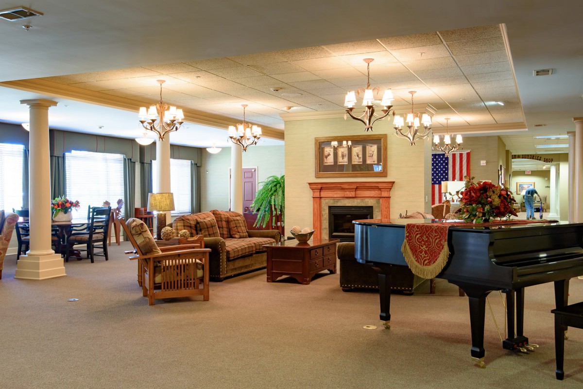 A spacious lobby featuring comfortable seating, a grand piano, chandeliers, and a fireplace with an American flag displayed on the wall.