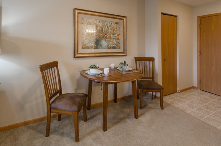 A cozy dining area with a wooden table set for two, accompanied by matching chairs and adorned with wall art.