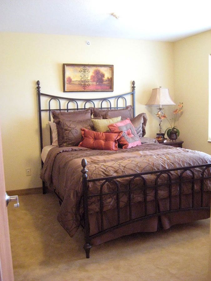 A cozy bedroom featuring a wrought-iron bed with plush pillows, a bedside lamp, and a framed painting above the headboard.