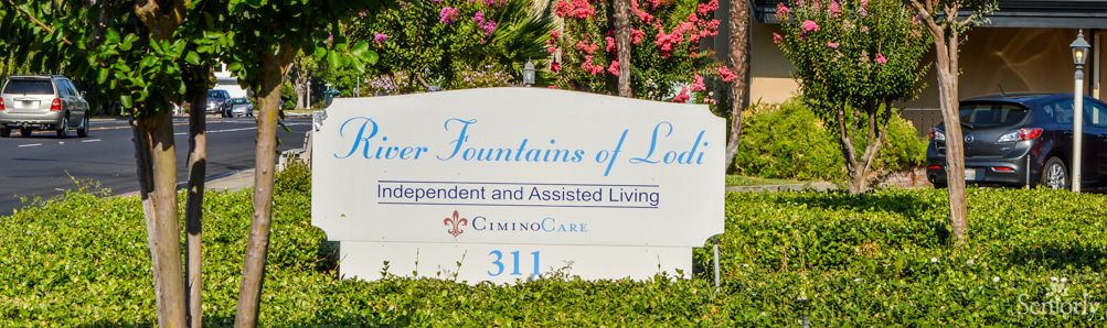A sign for River Fountains of Lodi, an independent and assisted living facility, surrounded by colorful flowers.