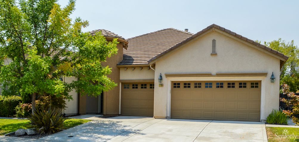 A suburban house with a three-car garage and a tree in the front yard.
