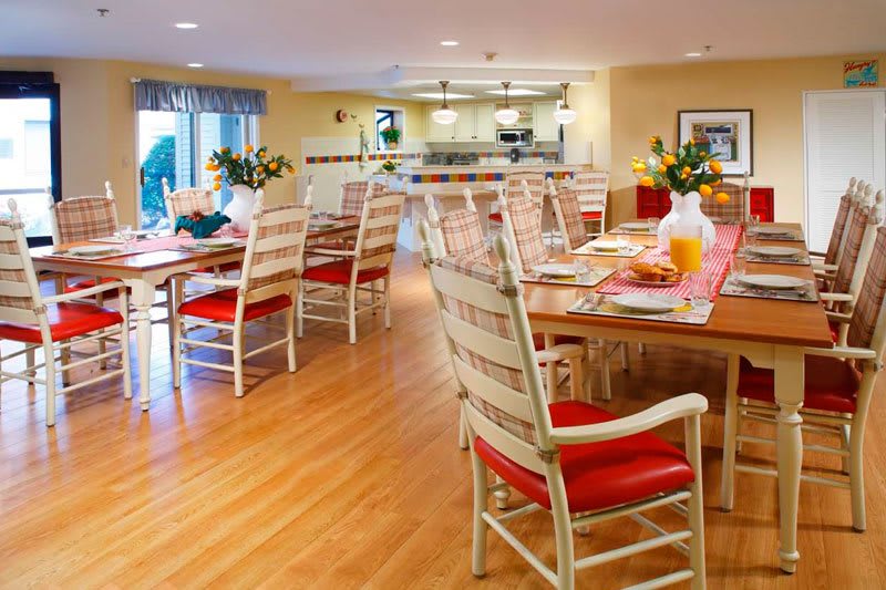 A cozy dining area with wooden chairs and tables, decorated with flowers and set for a meal.